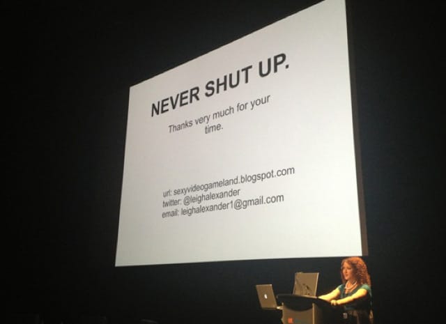 A large projection screen with the words "Never shut up" in large letters. The videogame writer Leigh Alexander stands at the podium.